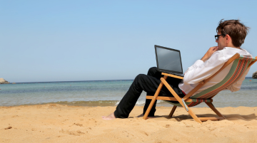 Man working on a laptop in a deckchair at the beach, indicating the flexibility with which exams may be delivered online